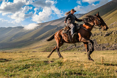 Rear view of a caucasian girl on a horse gallops through a mountain valley