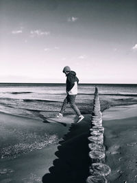 Teenage boy walking at beach against sky