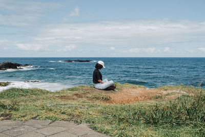 Rear view of woman sitting on rock at beach against sky