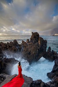 Rear view of woman standing on rock by sea against sky