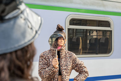 Woman holding mirror with friend reflection against train