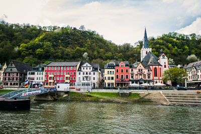 View of buildings by river against cloudy sky