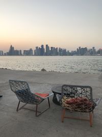 Deck chairs and tables by sea against sky during sunset