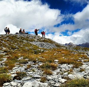 Tourists on mountain against cloudy sky