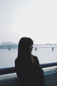 Young woman looking away while standing against river