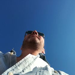 Directly below shot of man wearing sunglasses while standing against clear blue sky
