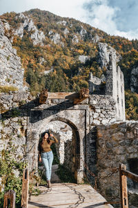 Young woman standing on footbridge of old castle ruin, autumn, fall, earth tones, style.