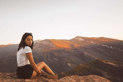 Young woman sitting on mountain against clear sky