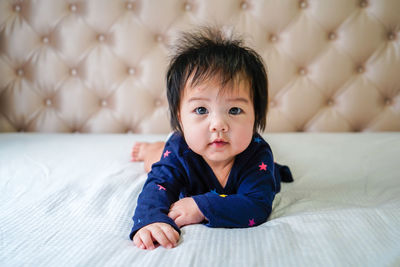 Cute little caucasian baby lying on bed at home,  smiling happily at camera in bright bedroom.