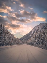 Road by snowcapped mountains against sky during winter