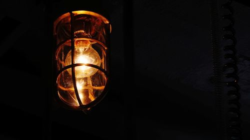 Close-up of illuminated light bulb hanging against black background