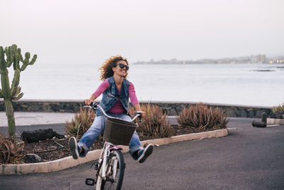 Cheerful woman riding bicycle on road against sea