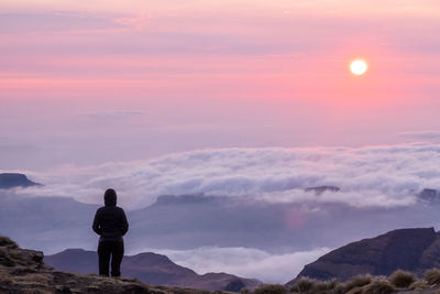 Rear view of woman standing on mountain against sky during sunset