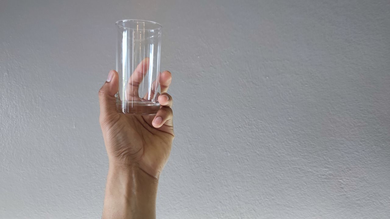 MIDSECTION OF PERSON HOLDING GLASS AGAINST WALL