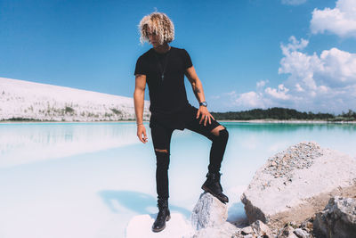 Full length of man on rock by lake against sky