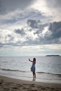 Woman taking selfie while standing on shore at beach against sky