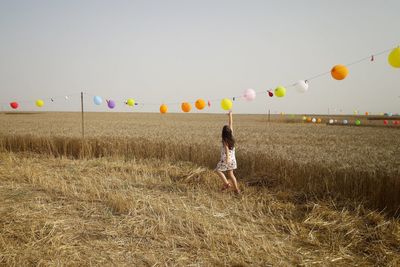 Girl with balloons on field against sky