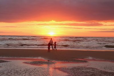 Silhouette people on beach against sky during sunset