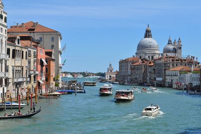 Boats in canal by buildings against sky in city