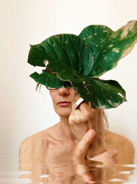 Close-up of woman with plant against wall