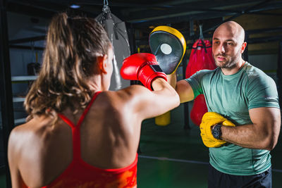 Young female boxer practicing with coach in gym