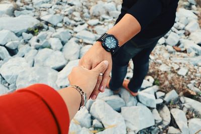Cropped image of woman holding man hand on rocks