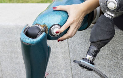 Unrecognizable crop female runner changing leg prosthesis for training while sitting on stone border in urban park