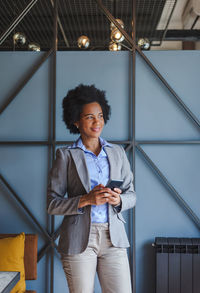 Smiling businesswoman using mobile phone while standing in cafe