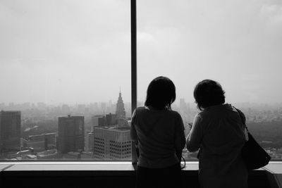 Rear view of women standing in front of building windows