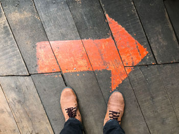 Low section of man standing on orange arrow sign on floorboard