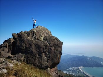 Man standing on rock against blue sky