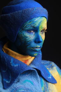 Close-up of young woman with painted face against black background