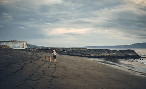 A woman running with the dogs on beach against sky