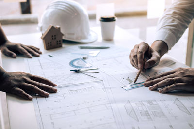 Cropped hands of male architects drawing blueprint at desk