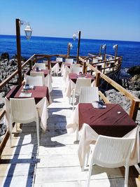 Empty chairs and table at beach against clear sky