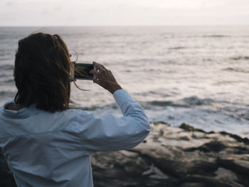 Woman taking a picture of the sunset over the ocean