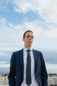 Young businessman in a suit and tie looking serious at camera standing outside in cloudy sky