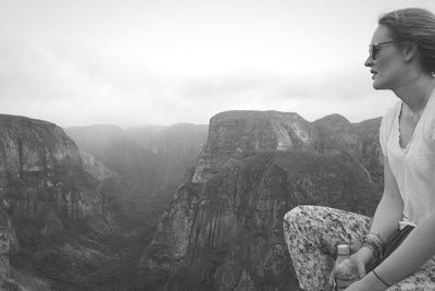 Woman sitting on rock by mountains against sky