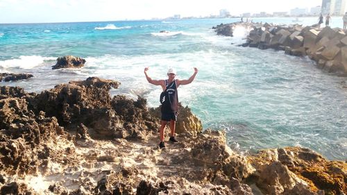 Rear view of man standing on rock by sea