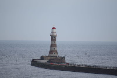 Lighthouse by sea against clear sky