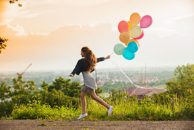 Rear view of woman holding balloons on field against sky