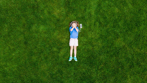High angle view of girl listening to headphones while lying on grassy field