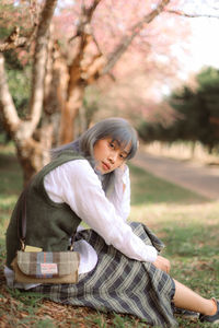 Full length of woman sitting against cherry tree