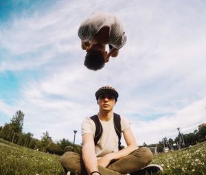 Portrait of young man sitting on grass against sky