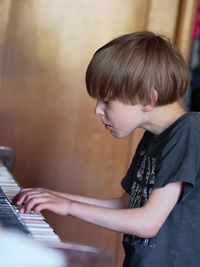 Side view of boy playing piano at home