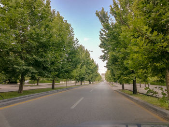 Empty road amidst trees against sky