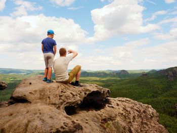 Father and son on mountain top watching into opened landscape. long forest valley up to horizon.