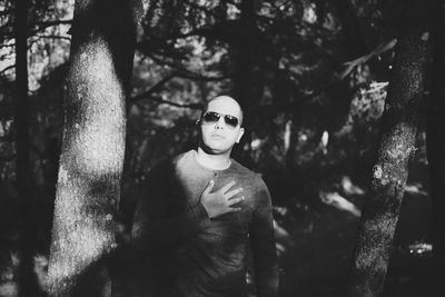 Young man standing by tree trunk in forest