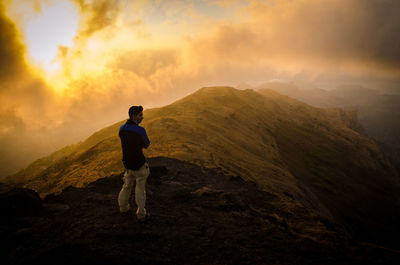 Rear view of man standing on mountain against sky