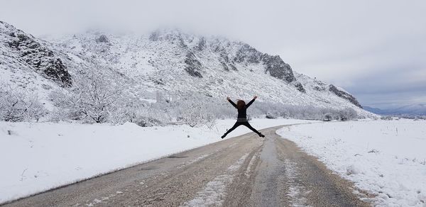 Rear view of woman jumping on road during winter